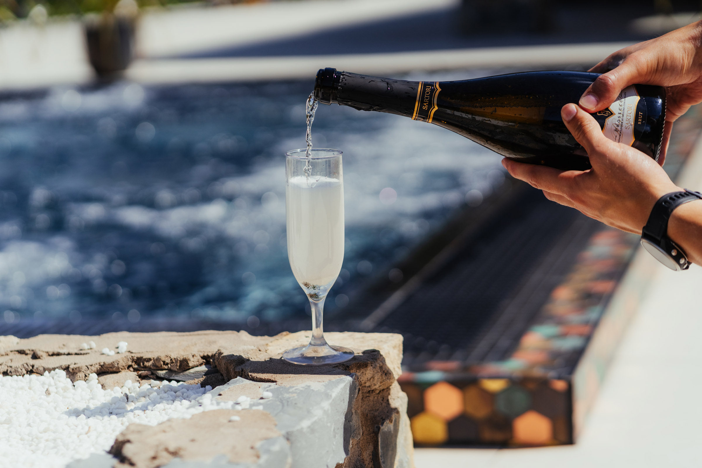 Champagne being poured into a glass next to pool